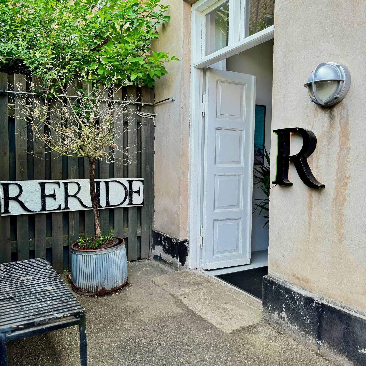 The Reride courtyard with an open white door, a RERIDE sign on the fence and a black R on the wall